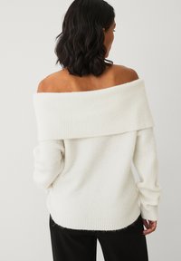 Off-shoulder, ribbet sweater i cremegul, med lange ærmer og en afslappet pasform, samt en blød, struktureret overflade.