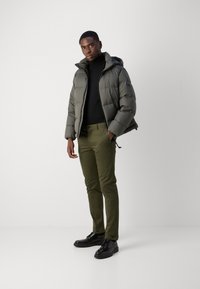 Pufferjack in donkergrijs, met een capuchon en horizontale naden, gecombineerd met olijfgroene chino's en zwarte veterschoenen. Minimalistisch ontwerp.