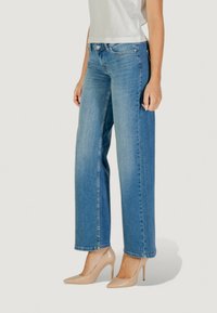 Jeans a gamba larga di un blu chiaro, realizzati in denim, con un classico design a cinque tasche e dettagli cuciti, abbinati a tacchi alti color nudo.
