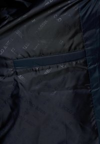 Tume sinise jope sisu, kus on korduv "U.S. POLO ASSN." logo trükk ja horisontaalne sisetasku õmmeldud servadega.