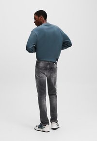Sudadera azul para hombres hecha de algodón, combinada con jeans grises desgastados y zapatillas blancas con acentos en azul y verde.