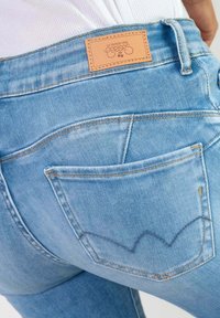 Lichtblauwe denim jeans met een leren merkpatch, voorzien van klassieke achterzakken en gele stikdetails. Versleten, gestructureerde afwerking.