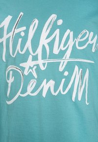 Jasnoniebieska koszulka z dużym białym napisem "Hilfiger Denim" oraz grafiką gwiazdki, wykonana z miękkiego materiału bawełnianego.