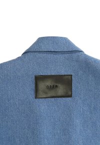 Jasnoniebieska kurtka dżinsowa z czarną skórzaną metką z napisem "OPRA" wyszytym na tylnym kołnierzu. Miękka tekstura i klasyczny design kołnierza.