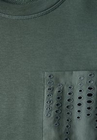 Sweatshirt vert avec col rond, texture côtelée et poche poitrine ornée de broderies en œillet délicates. Tissu doux avec une finition lisse.