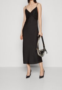 Robe nuisette en satin noir avec bordure en dentelle, bretelles spaghetti et coupe mi-longue. Associée à un sac métallique et des escarpins noirs à bout pointu.