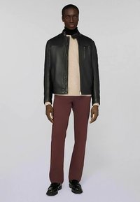 Czarna skórzana kurtka na zamek, kremowy sweter, bordowe spodnie i czarne buty. Kurtka ma usztywnioną konstrukcję i minimalną ilość metalowych elementów.