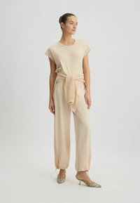 Top beige con maniche corte e pantaloni a vestibilità ampia. I pantaloni presentano una cintura legata e dettagli testurizzati. Indossati con tacchi con motivo.