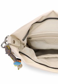 Beżowa torba materiałowa z wewnętrzną kieszenią na zamek, srebrnymi elementami i kolorowym breloczkiem. Gładka tekstura, przestronne wnętrze.