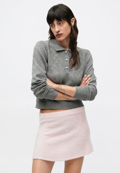 Šedý pletený sveter s golierom polo, diamantovými vzormi a perlovými gombíkmi; doplnený o mäkkú ružovú mini sukňu s hladkou textúrou.
