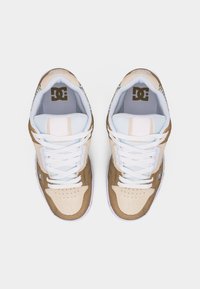 Ζευγάρι μπεζ και καφέ παπουτσιών DC με λευκά κορδόνια και επενδυμένες γλώσσες, φωτογραφημένα από πάνω σε λευκό φόντο.