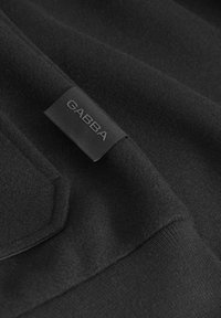 Črna obleka z gladko teksturo in večplastnim dizajnom; na tkanini je vidna poudarjena oznaka GABBA.