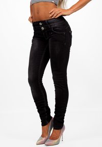 Jeans skinny negros con una cintura alta, costuras decorativas y dos bolsillos frontales. Combinados con zapatos de tacón altos y brillantes.