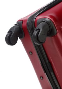 Maleta rígida roja con superficie texturizada, ruedas negras y cierre con cremallera en el lateral. Diseño robusto para viajar.