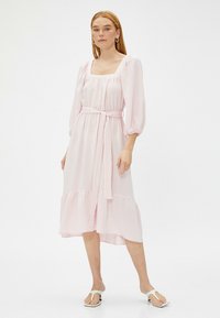 Hellrosa Midi-Kleid mit quadratischem Ausschnitt, Puffärmeln und einem Gürtel in der Taille, aus strukturiertem Stoff mit gestuftem Rüschensaum.