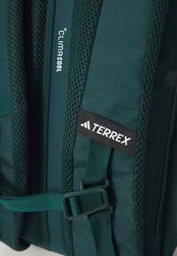 Zeleni ruksak s teksturiranom površinom, mrežastim detaljima, podesivim trakama i crnim oznakom "TERREX". Sadrži ClimaCool tehnologiju.