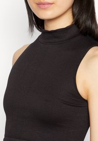 Top preto sem mangas, com textura canelada e gola alta, exibindo um design justo e detalhes de costura mínimos.
