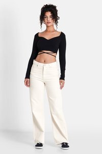 Top corto a maniche lunghe nero a coste con scollatura a cuore. Abbinato a jeans ampi di colore bianco sporco con orli sfrangiati e chiusura a bottone.