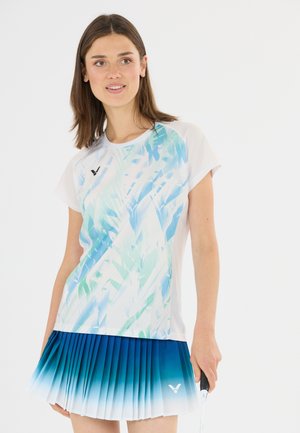 Ung kvinde iført en hvid og blå mønstret sportstrøje og en blå gradient plisseret nederdel, der holder en badmintonketsjer.