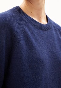 Marineblauwe gebreide trui met een ronde hals, geribbelde rand en raglanmouwen. Gemaakt van zachte stof met een gladde textuur.