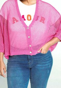 Rosa nätcardigan med V-halsdesign, som har små knappar och öppen front. Bärs över en vit skjorta med färggd "AMOUR"-text.