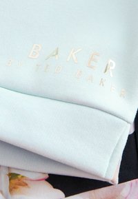 Lichtblauw sweatshirtstof met een glanzend gouden "BAKER by TED BAKER" logo. Opvallend detail zijn de stiksels en de soepele textuur.