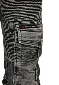 Pantalons cargo en denim noir avec un motif rayé texturé, dotés d'une poche latérale et d'une étiquette de marque. Accents en matériel argent standard.