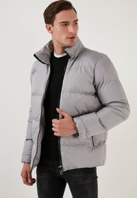Pilkas pūkinis švarkas su aukštu apykakle, užtrauktuku ir šoninėmis kišenėmis. Ypatumai: siuvinėta konstrukcija ir glotnus, lengvas audinys.