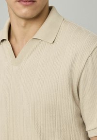 Polo en maille beige avec col en V et manches courtes, présentant des rayures texturées et un col côtelé.