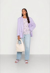 Blazer oversized de lavanda sobre uma blusa floral, combinado com jeans azul claro e sandálias lilás de salto; segurando uma bolsa bege.