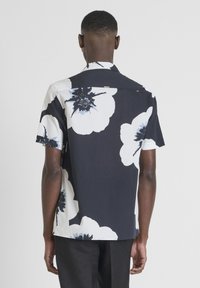 Camicia a maniche corte realizzata in tessuto leggero con uno sfondo nero e ampi motivi floreali bianchi e blu. Presenta un colletto classico e un parte posteriore con yoke.