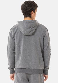 Grauer Kapuzenpullover aus weichem Material, mit einer Kordelzugkapuze, gerippten Bündchen und einem gerippten Saum, sowie Druckakzenten am linken Ärmel.