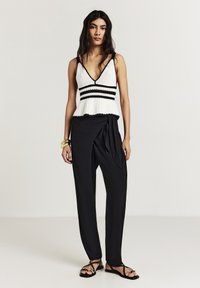 Top a righe bianche e nere con peplum, abbinato a pantaloni larghi neri avvolgenti e sandali neri piatti. Design e trama semplici e leggeri.
