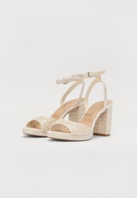 Beige augstpapēžu sandales ar atvērtām pirkstiem, rotātas ar rhinestones. Ir siksna ar sprādzi un teksturēta blokveida papēdis.