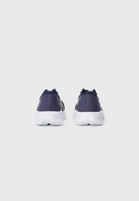 Baskets de sport navy avec une tige texturée, rehaussées de rayures jaunes vives, dotées d'une semelle blanche rembourrée et d'un col rembourré.