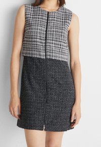 Robe sans manches élégante avec un haut à carreaux gris texturé et un bas gris foncé uni, dotée d'un zip frontal et d'une silhouette ajustée.
