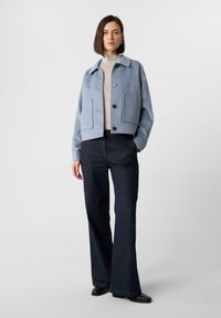 Jasnoniebieska krótka kurtka z dużymi kieszeniami z przodu, zapięcie na guziki, pod nią szary golf, w połączeniu z ciemnymi szerokimi spodniami.