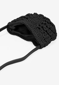 Bolso de mano de ganchillo negro con un exterior texturizado, forro negro liso y tirantes ajustables. Cierre con cremallera en la parte superior.