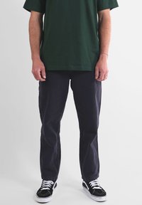 T-shirt en coton vert, coupe décontractée; pantalon bleu marine foncé à coupe droite; baskets noires et blanches avec lacets et semelles texturées.