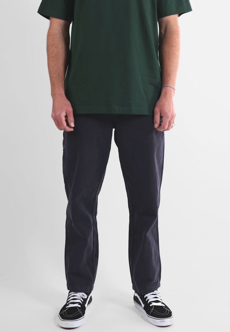 T-shirt en coton vert, coupe décontractée; pantalon bleu marine foncé à coupe droite; baskets noires et blanches avec lacets et semelles texturées.