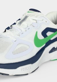 Άσπρο αθλητικό παπούτσι με πράσινο σήμα Nike, σκούρες μπλε λεπτομέρειες, λευκά κορδόνια και ετικέτα "Structure Plus" στη γλώσσα.