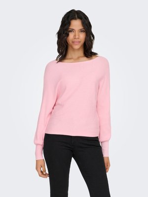 Svetlo roza rebrasti pulover z širokim izrezom in dolgimi, rahlo napihnjenimi rokavi. Nošen s črnimi hlačami, vidna tekstura tkanine.