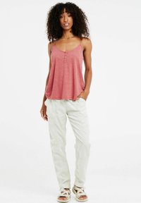 Top rosso senza maniche con scollatura a girocollo e tre bottoni decorativi, abbinato a pantaloni cargo chiari e sandali con cinturini.