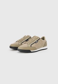 Beige treningsko med en glatt tekstiloverdel, svarte detaljer, klassisk snøring, og en teksturert gummisåle.