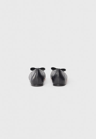 Ballerines noires en cuir texturé, avec un motif matelassé et des nœuds sur les talons. Semelle lisse et design à bout arrondi.