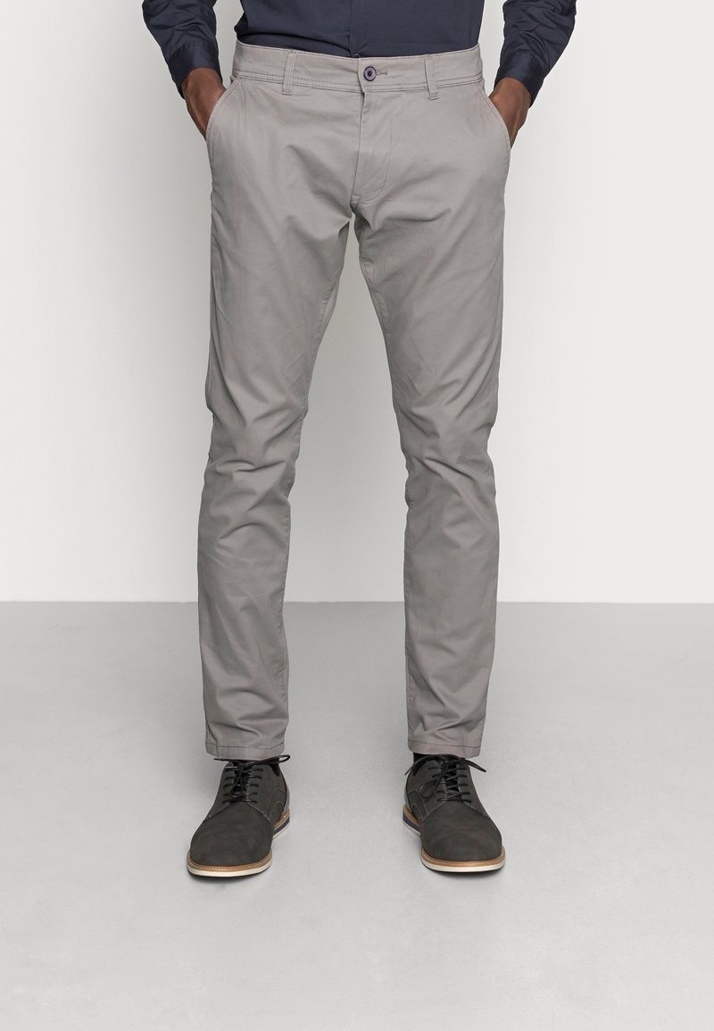 Šedé chino kalhoty se slim fit, předními kapsami a zapínáním na knoflík. Nosí se s tmavými botami s bílou podrážkou.