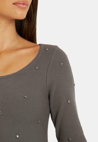 Szary, prążkowany top z długim rękawem, z dekoltem w serek, ozdobiony metalicznymi akcentami rozmieszczonymi po całej tkaninie.