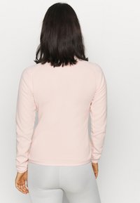 Haut rose clair à manches longues en tissu doux, présentant un design ajusté et un col rond. Manches se terminant au poignet avec des poignets côtelés.