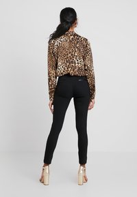 Bluzka w panterkę z długimi rękawami, zestawiona z dopasowanymi czarnymi spodniami. Spodnie mają kieszenie na zamek i długość do kostek.