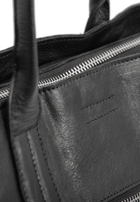Borsa a tracolla in pelle nera con finitura testurizzata, zip argentata e doppi manici. I dettagli includono cuciture ordinate e un design semplice.